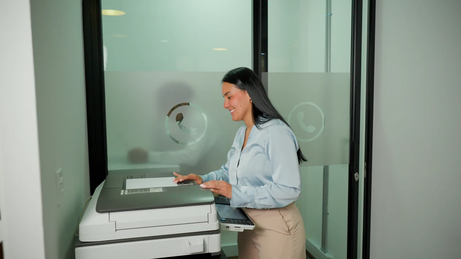 Une femme numérise des documents avec une imprimante multifonction dans un bureau.