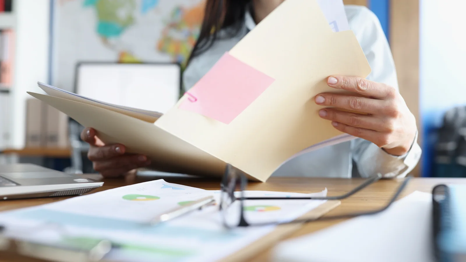 Une personne consulte un dossier papier à son bureau, près d’un ordinateur et de documents.