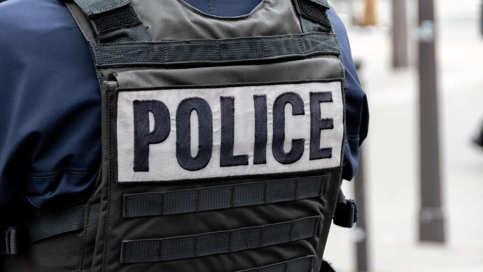 Inscription POLICE sur le gilet pare-balles d’un policier vu de dos.