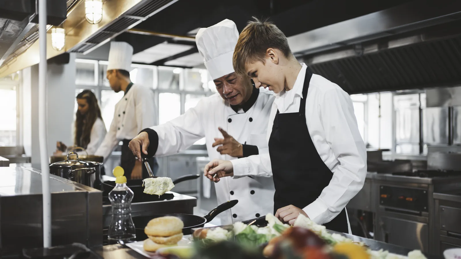 Un professeur accompagne un élève pendant un atelier de cuisine.