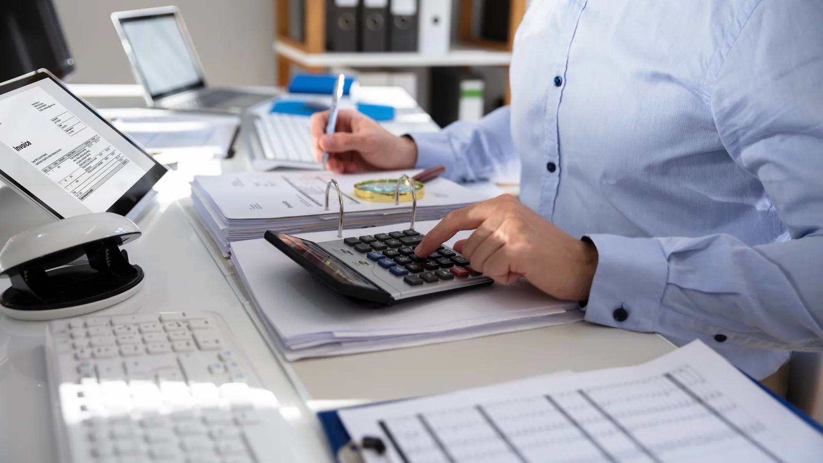Une personne utilise une calculatrice en consultant des documents comptables à son bureau.