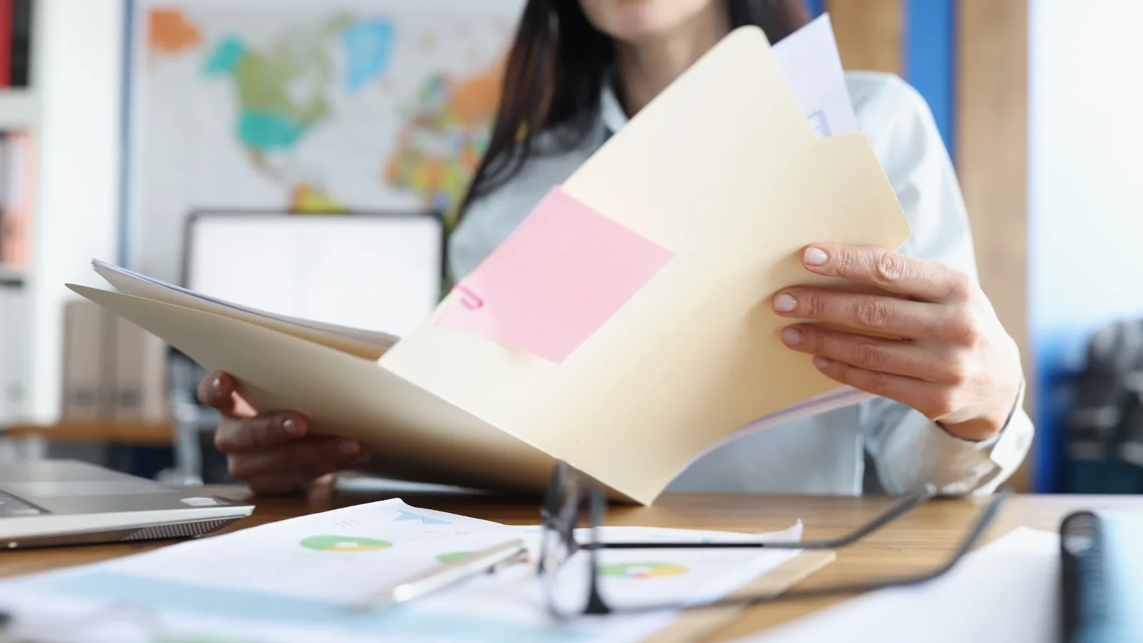 Une personne examine des documents et un dossier papier à son bureau, près d’un ordinateur.