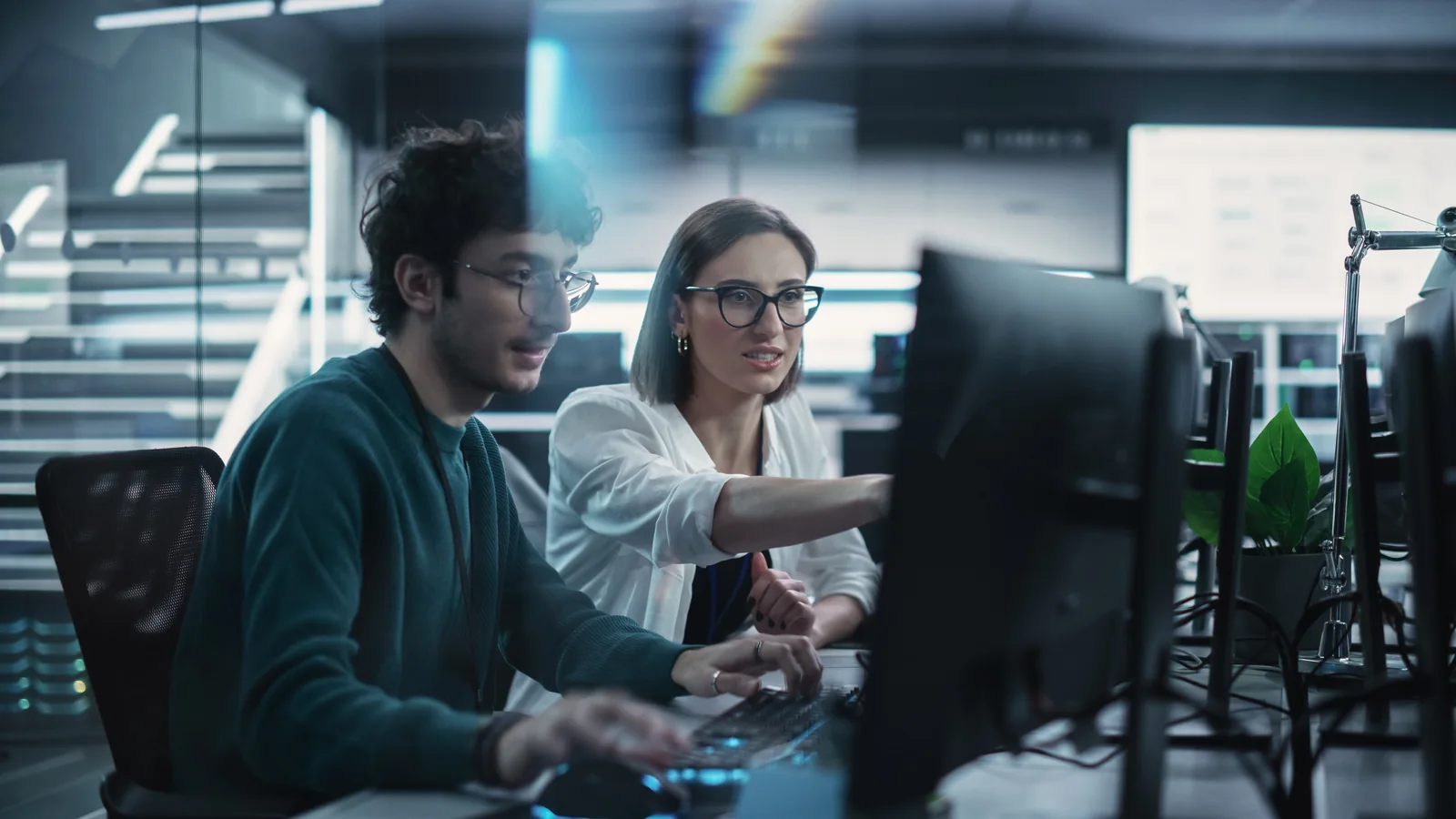 Deux collègues travaillent devant des écrans dans un bureau informatique.