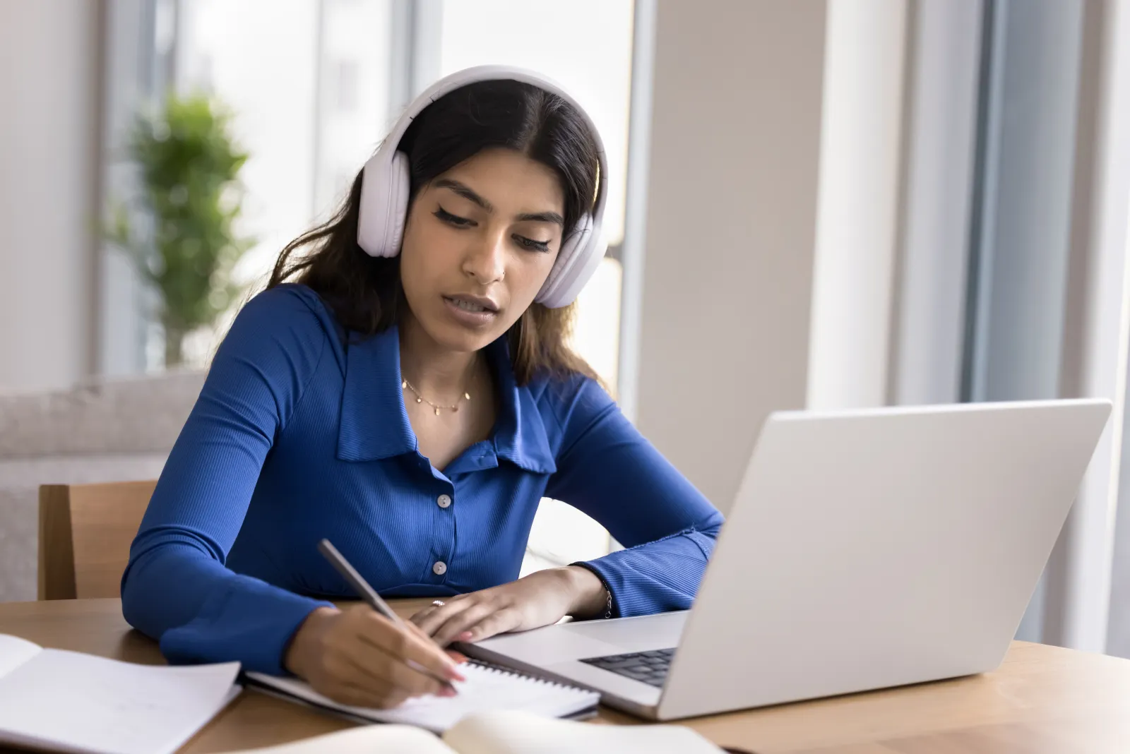 Une étudiante portant un casque audio prend des notes devant un ordinateur portable.