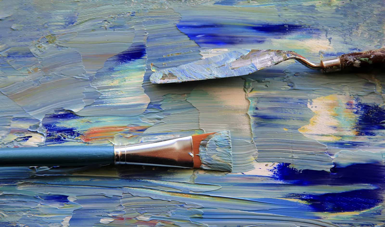 Un pinceau et un couteau à peindre reposent sur une palette couverte de couleurs.