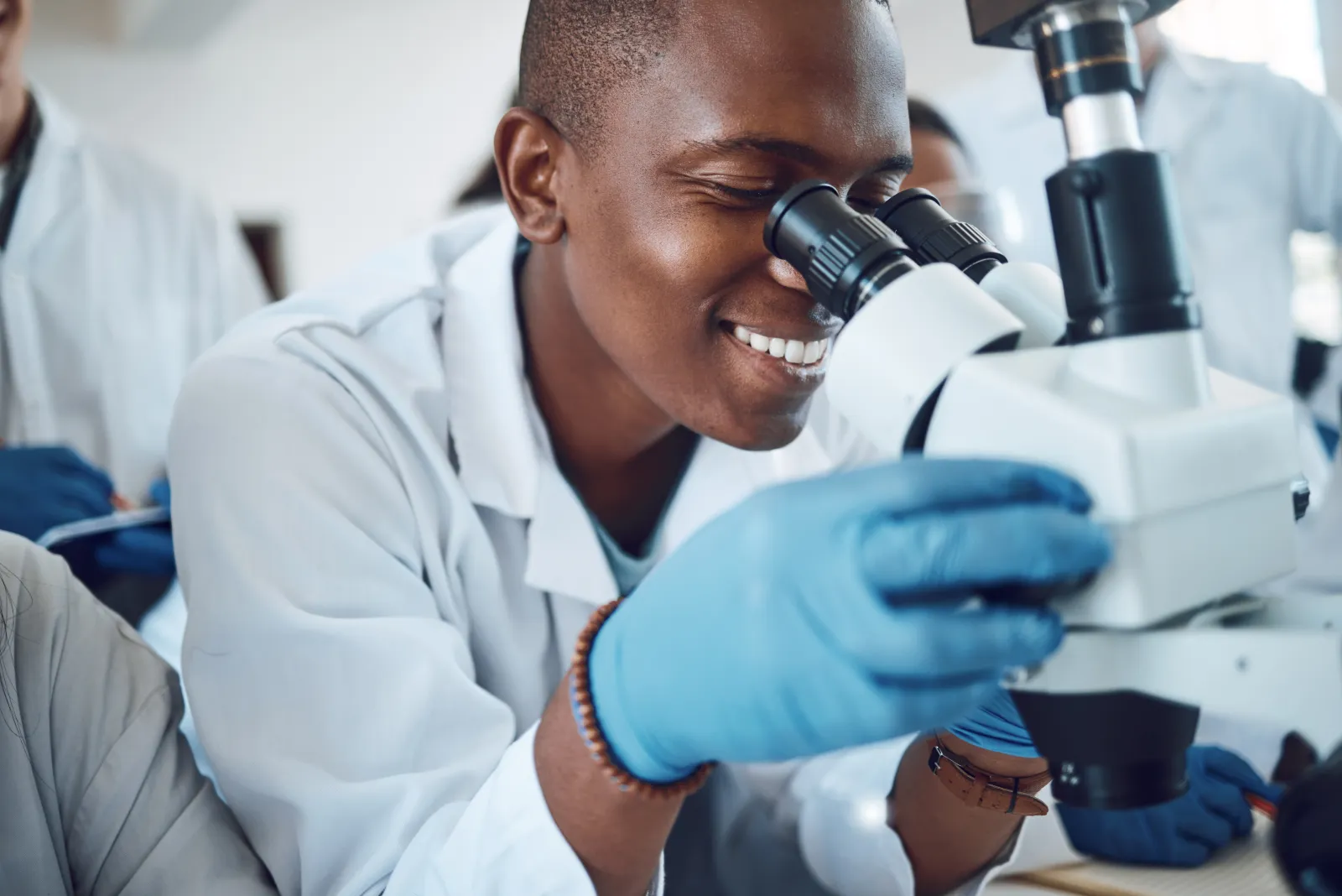 Une personne en blouse observe un échantillon au microscope dans un laboratoire.