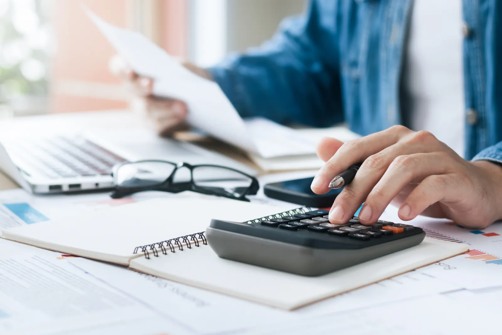 Une personne utilise une calculatrice en consultant des documents financiers.