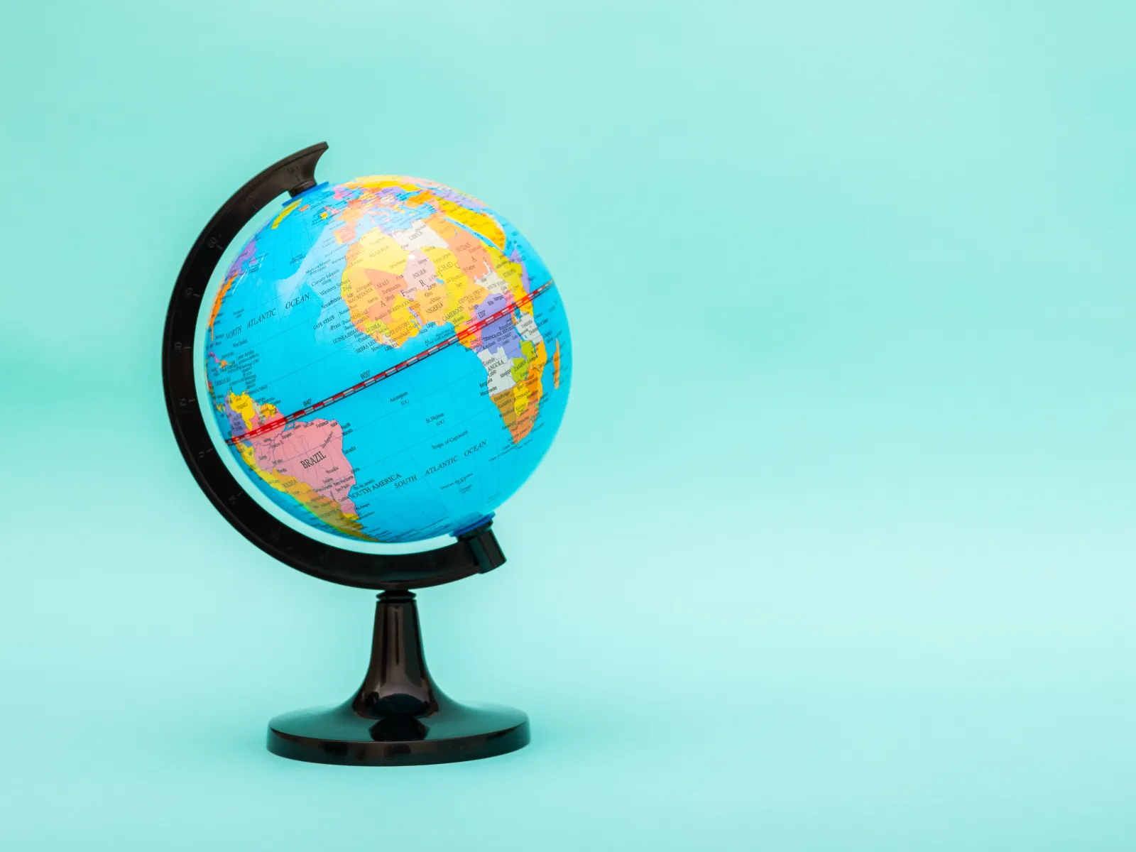 Un globe terrestre sur son support, devant un fond turquoise.