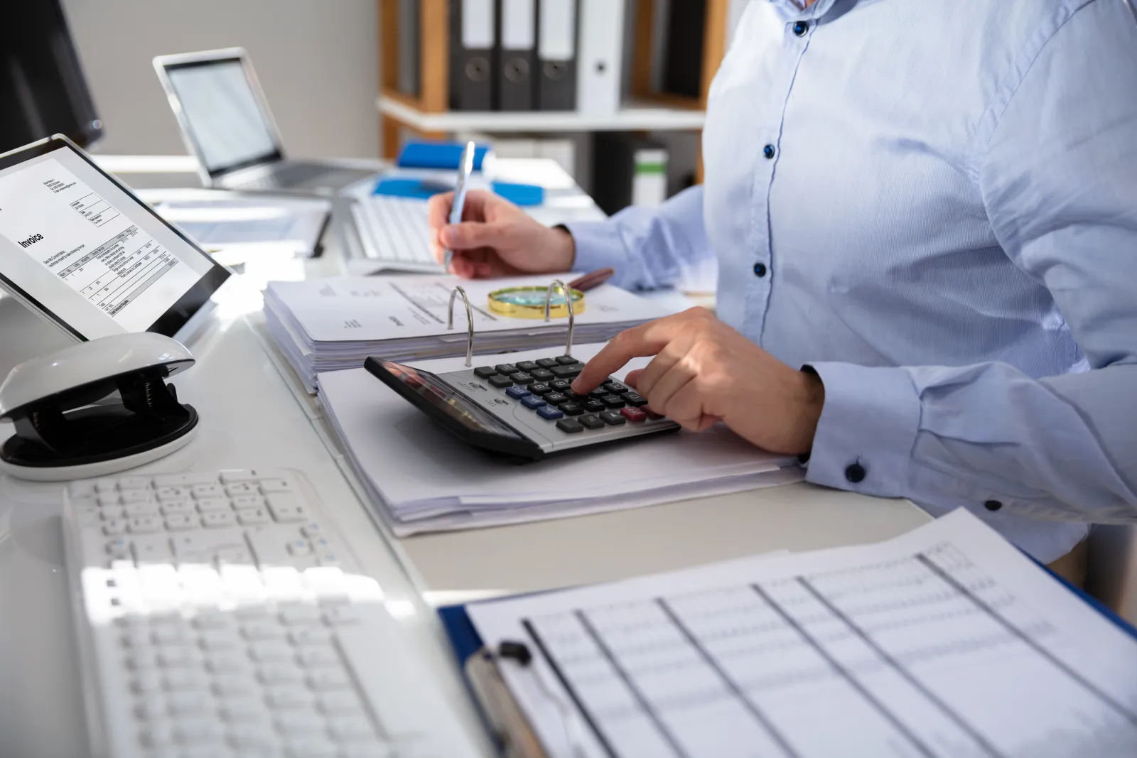 Une personne vérifie des documents comptables avec une calculatrice et un stylo.