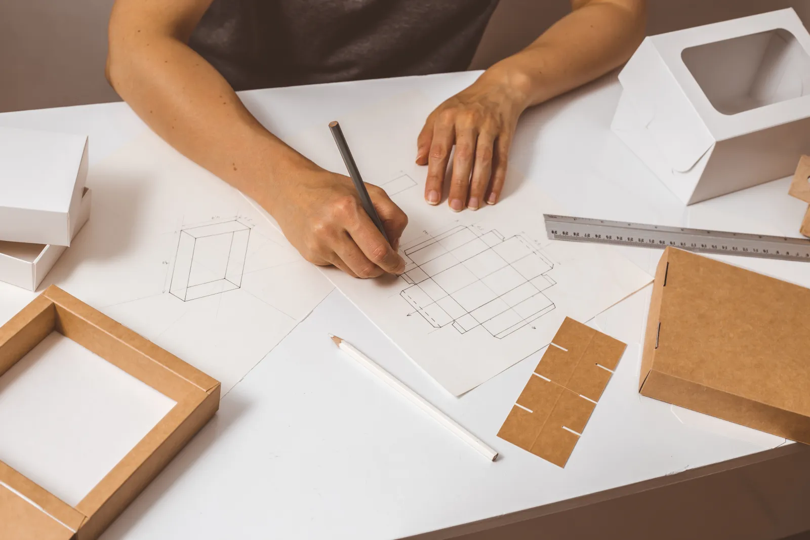 Une personne dessine le patron d’un emballage à côté de maquettes en carton.