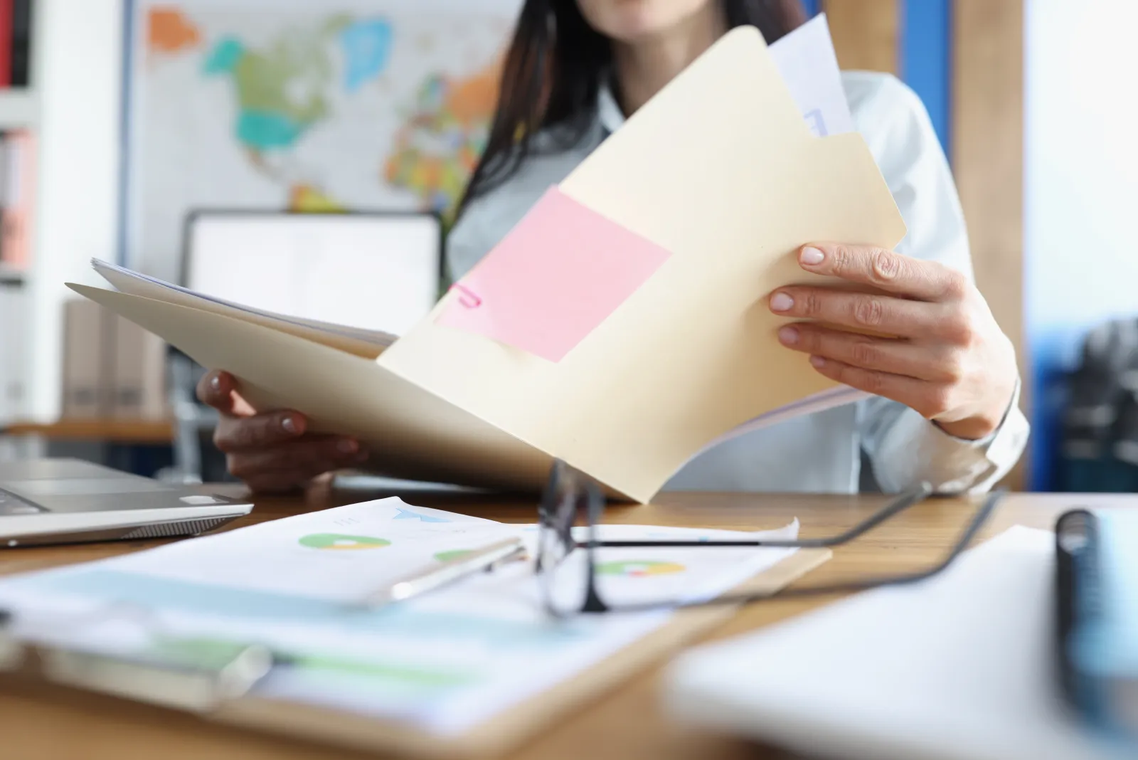 Une personne examine un dossier papier à son bureau, près d’un ordinateur.