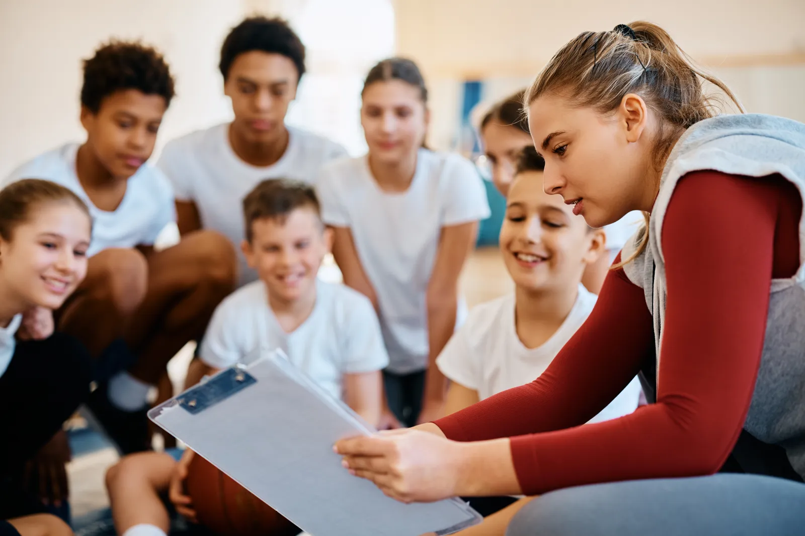 Une entraîneuse présente des consignes à un groupe de jeunes sportifs dans un gymnase.