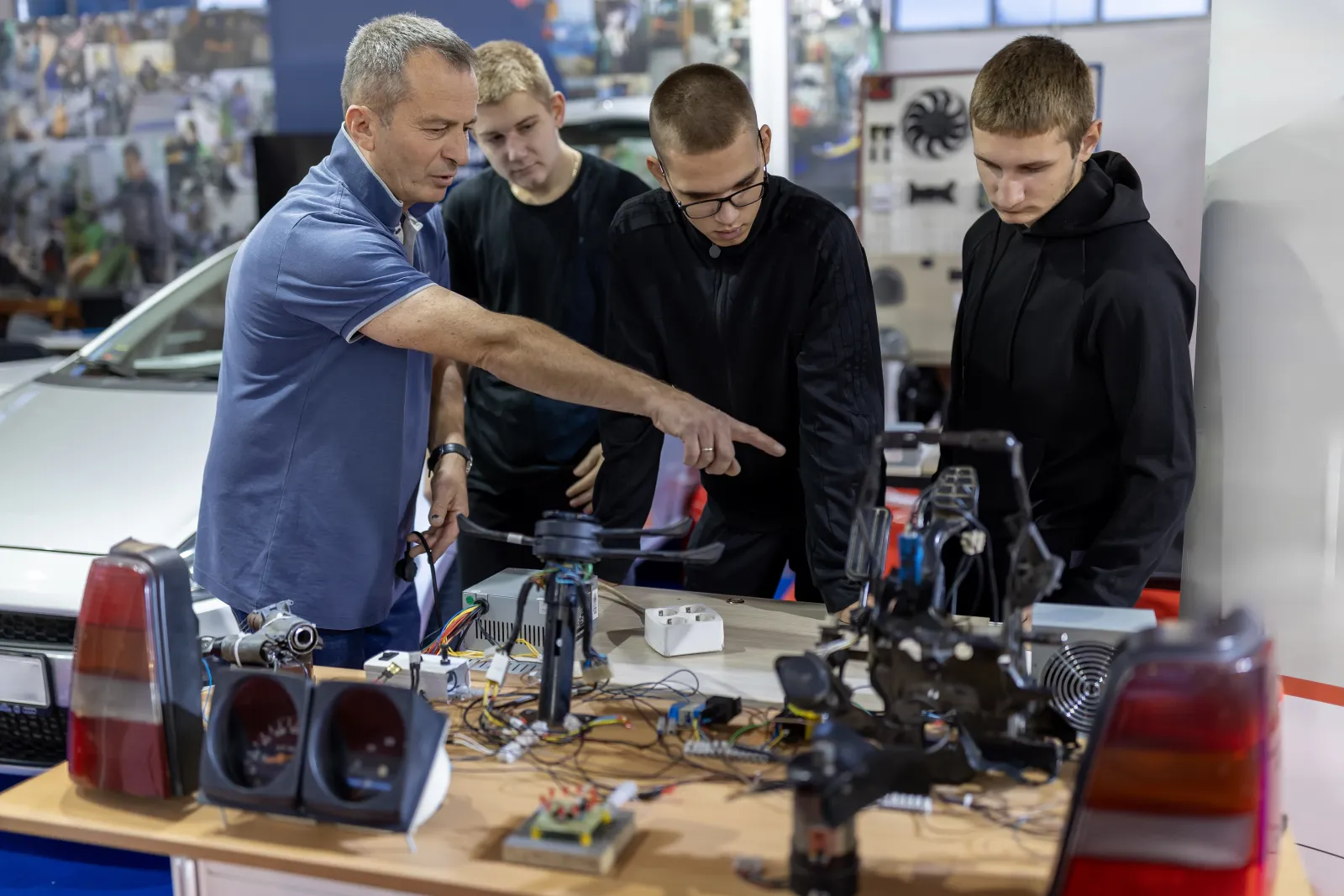 Un enseignant explique le fonctionnement de composants automobiles à trois élèves dans un atelier.