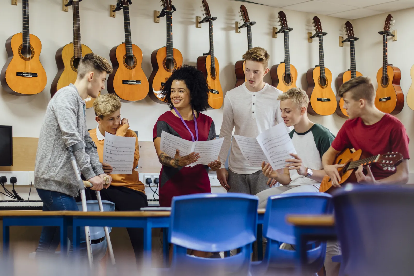 Une enseignante accompagne un groupe d’adolescents qui chantent, partitions en main, dans une salle de musique.