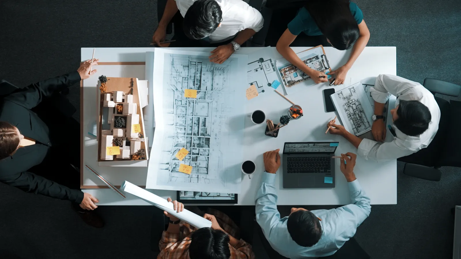 Une équipe travaille autour d’une table couverte de plans et d’une maquette de bâtiment.