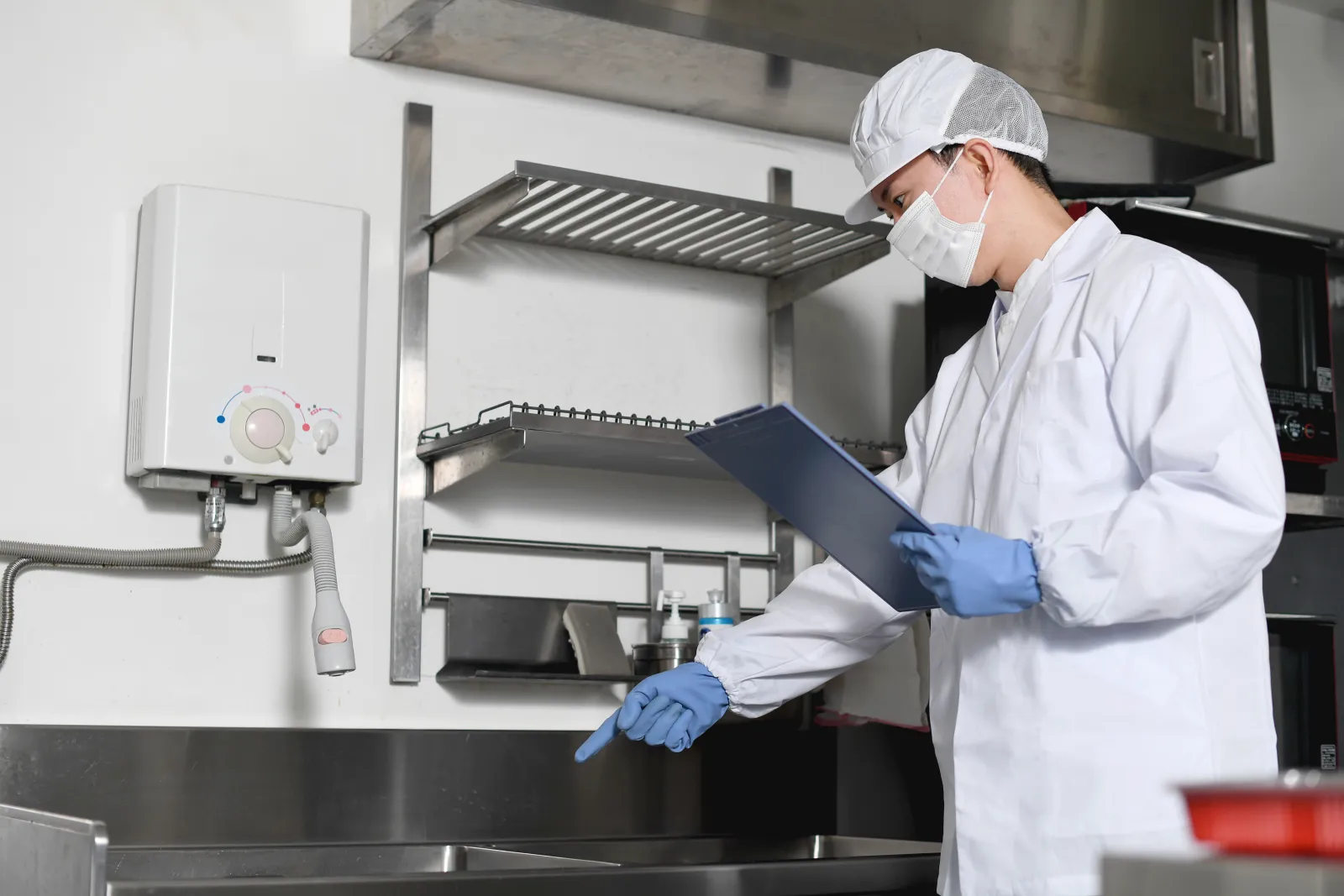 Un professionnel en tenue de protection contrôle les équipements d’une cuisine.