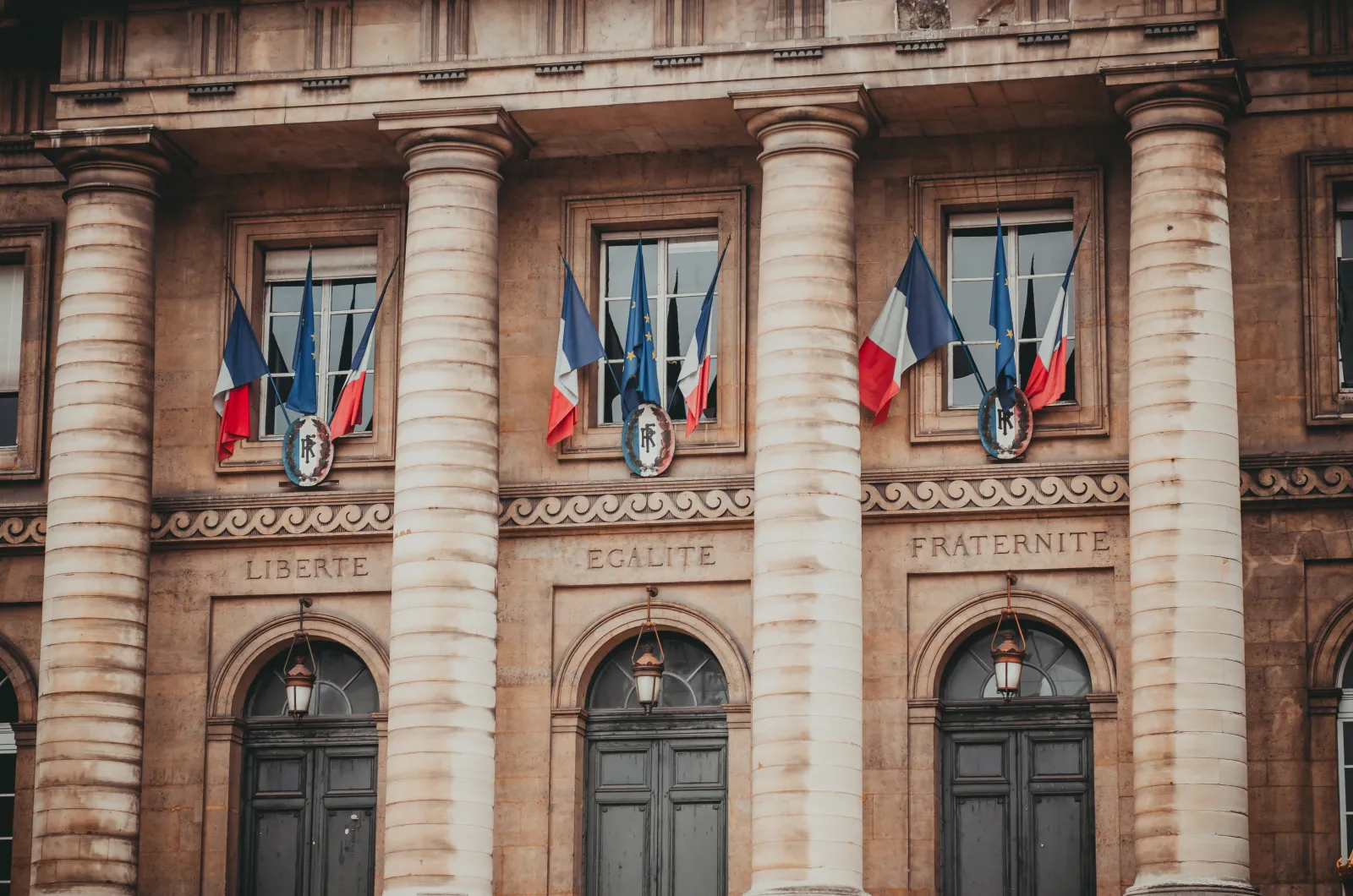 Façade d’un bâtiment public parisien ornée de drapeaux français.