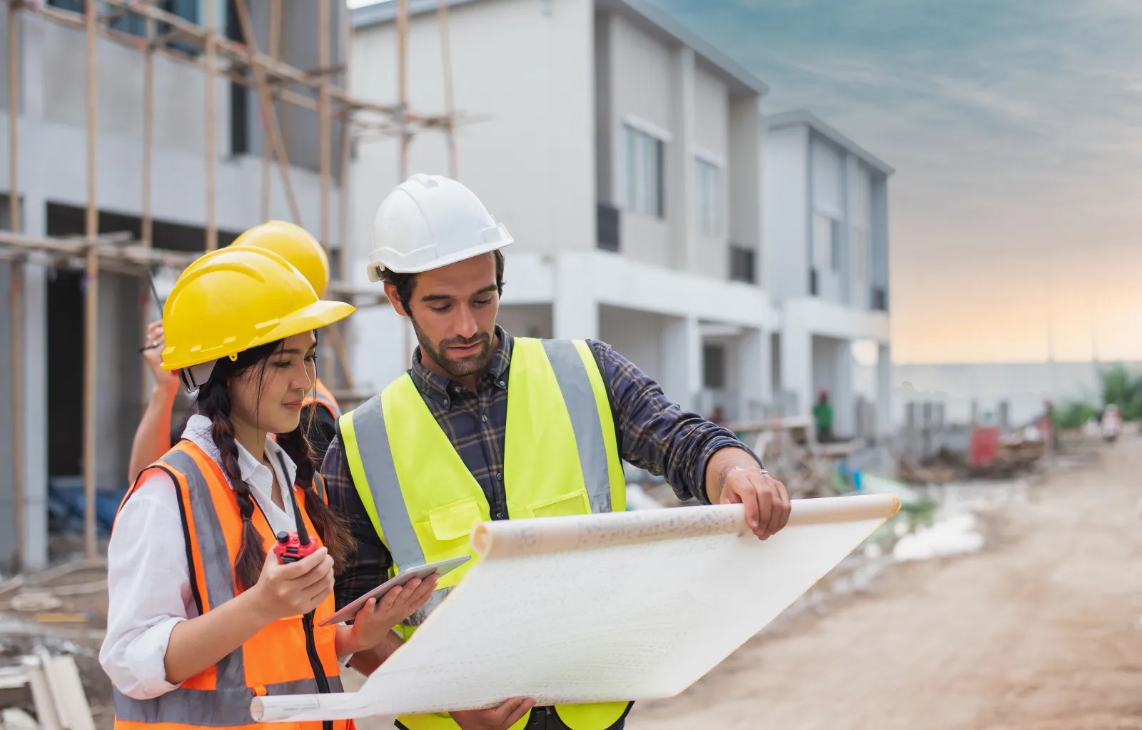 Deux professionnels portant un casque et un gilet de sécurité consultent un plan sur un chantier.