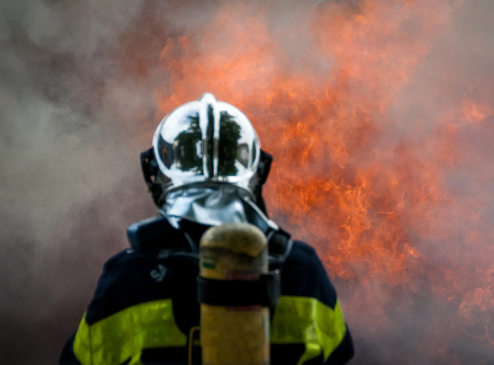 Un pompier équipé d’un casque et d’un appareil respiratoire fait face à des flammes.