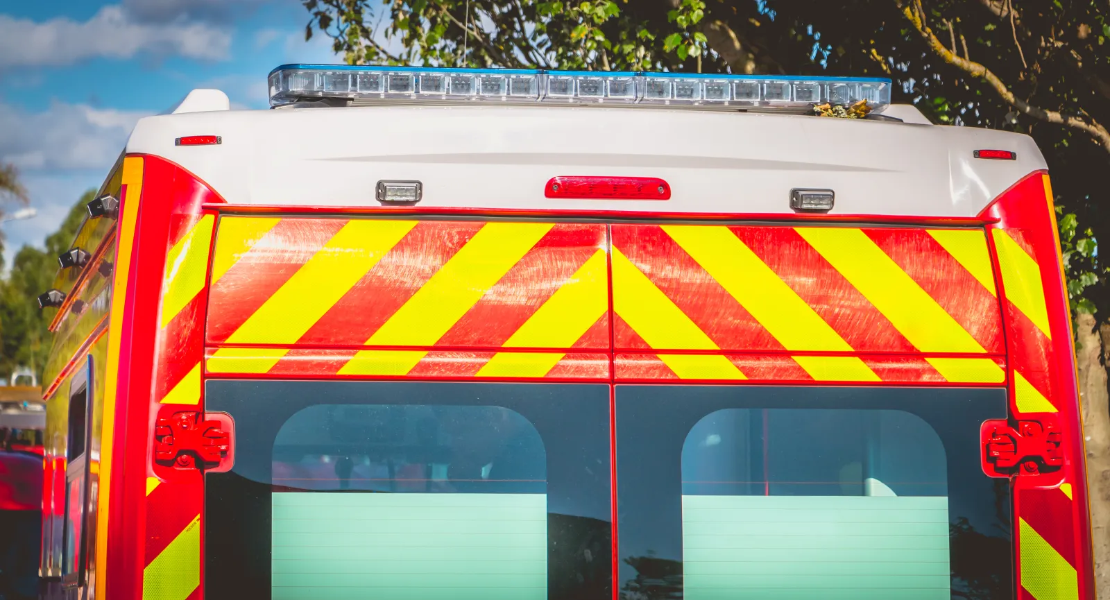Arrière d’un véhicule de secours rouge, avec des bandes jaunes et un dispositif lumineux.