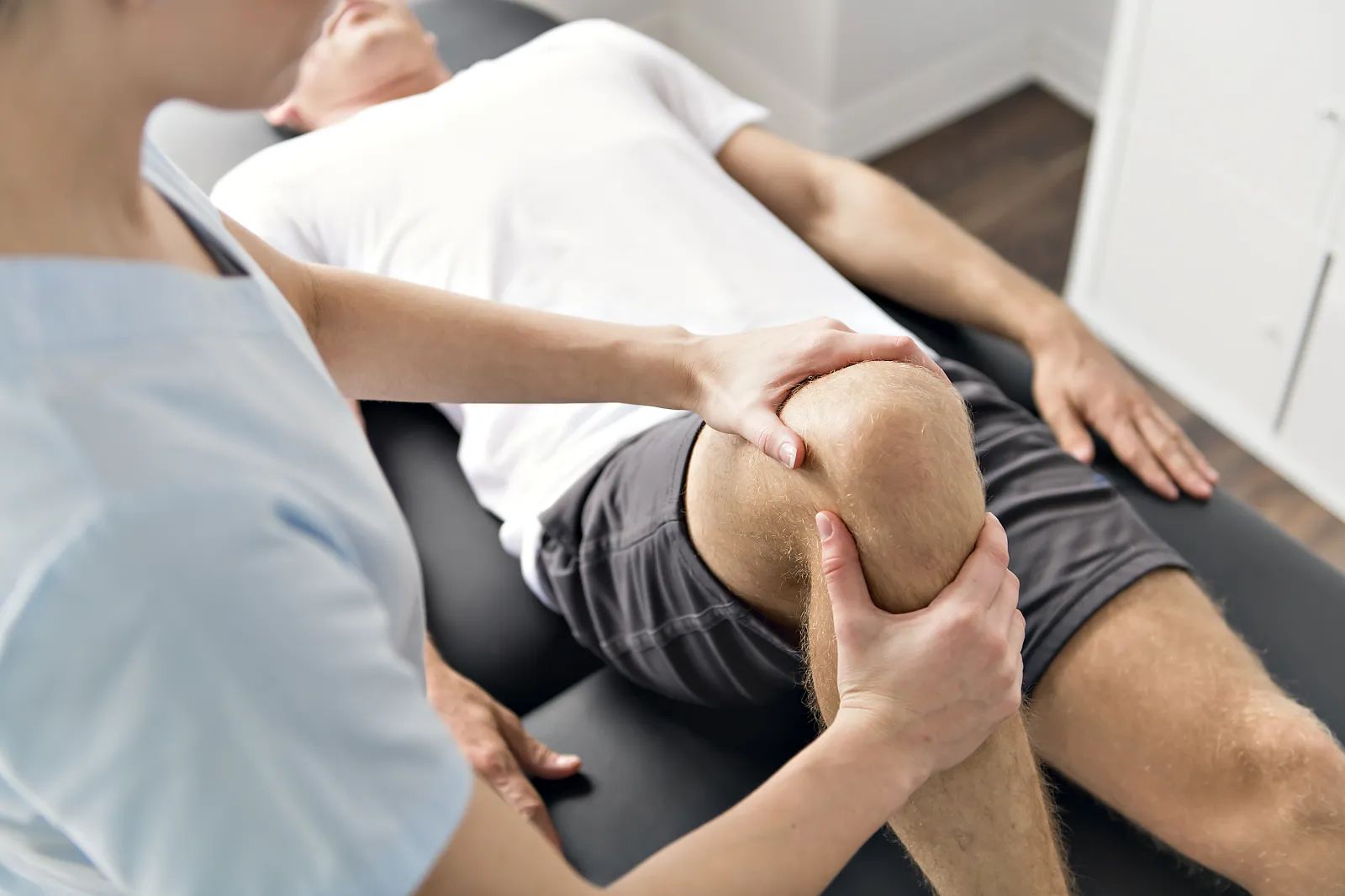 Une professionnelle accompagne le mouvement du genou d’un patient allongé.