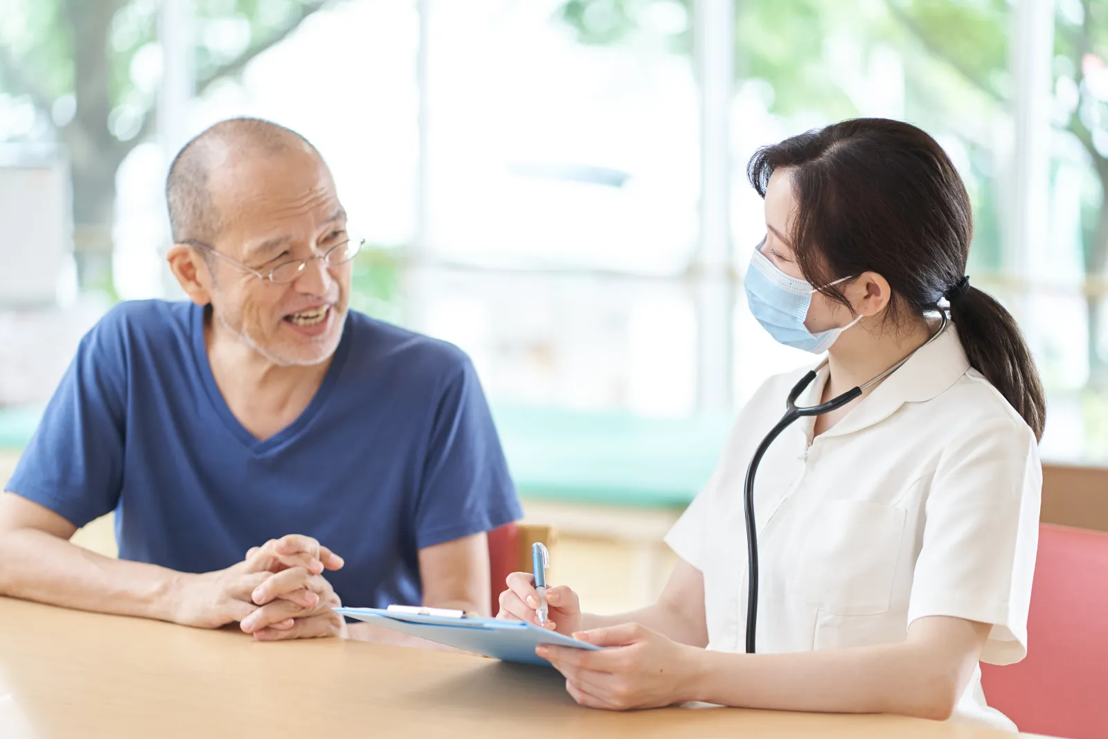 Une professionnelle de santé échange avec une personne âgée et prend des notes.