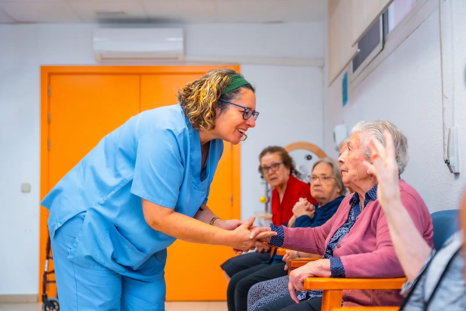 Une soignante tient la main d’une femme âgée assise dans un fauteuil.