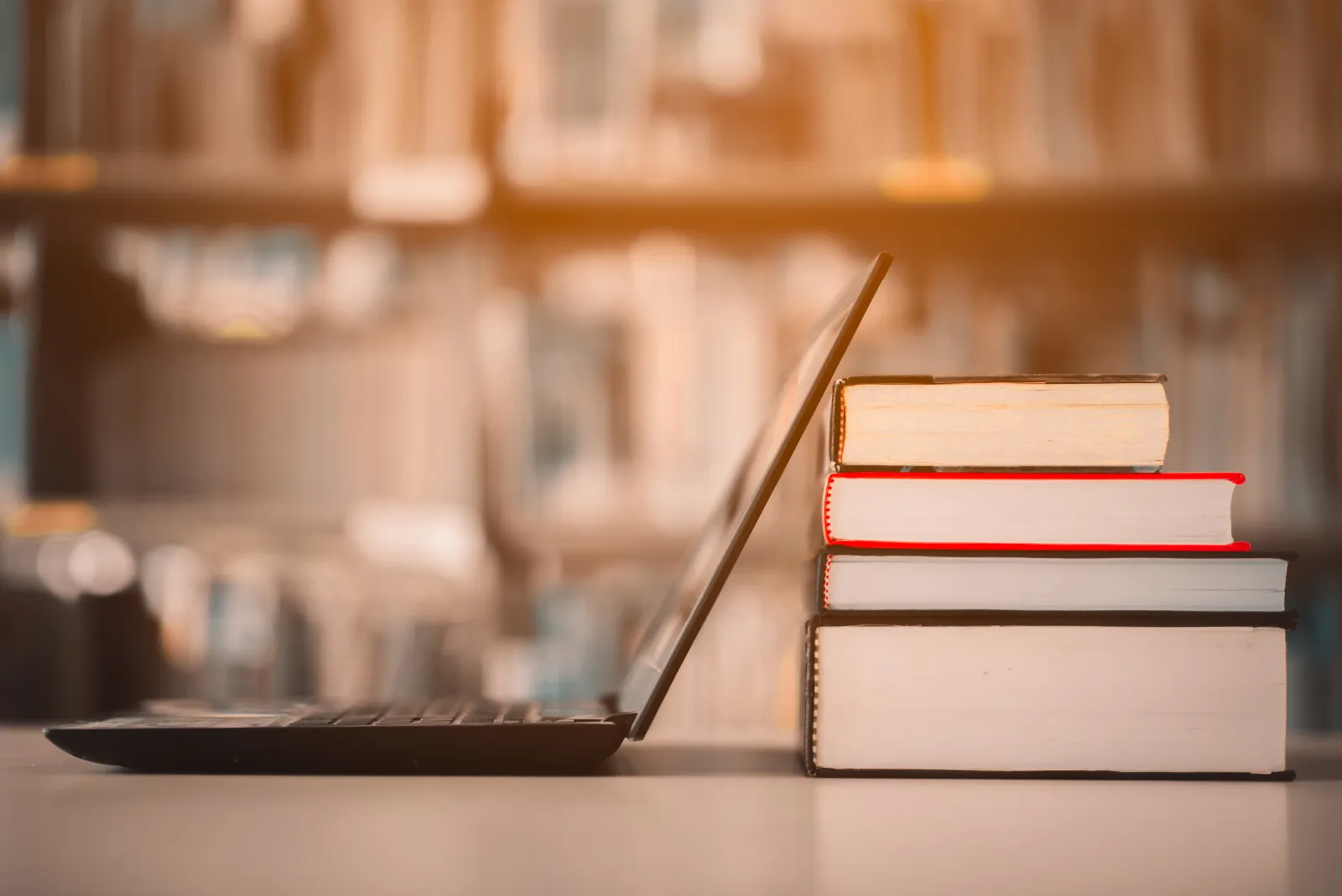 Un ordinateur portable et plusieurs livres sont posés sur une table de bibliothèque.